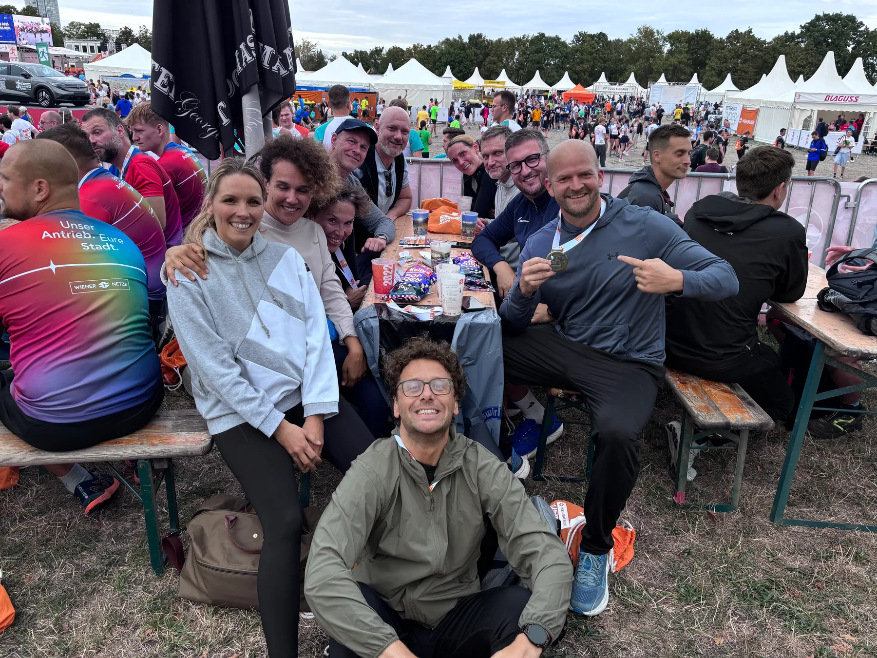 Das Team am Tisch beim Business Run – ein Kollege zeigt seine Medaille
