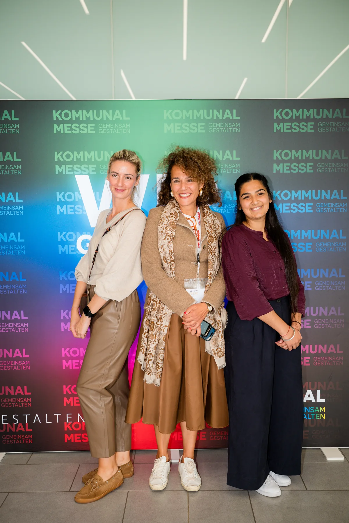 Zu dritt vor der bunten Fotowand der KOMMUNAL Messe 2026